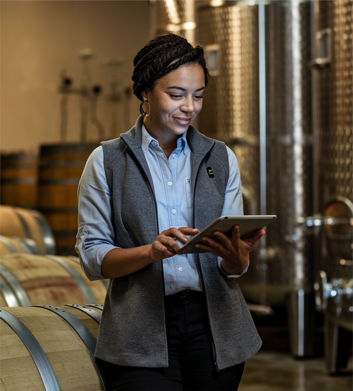 A winemaker reviewing fermentation data on a tablet while standing in the cellar